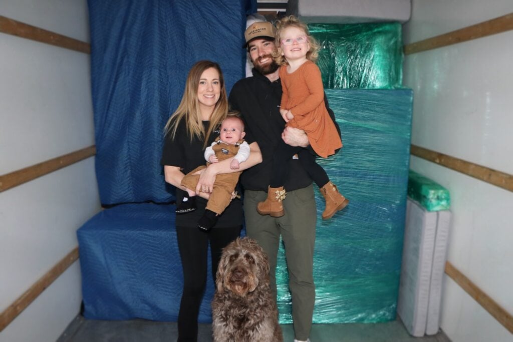 The Harrington family and their dog inside a moving truck beside protected furniture